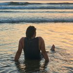 Man laying in the sea looking at sunset on a beach