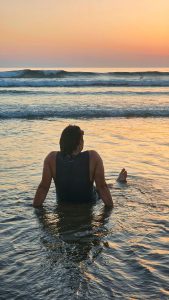 Man laying in the sea looking at sunset on a beach