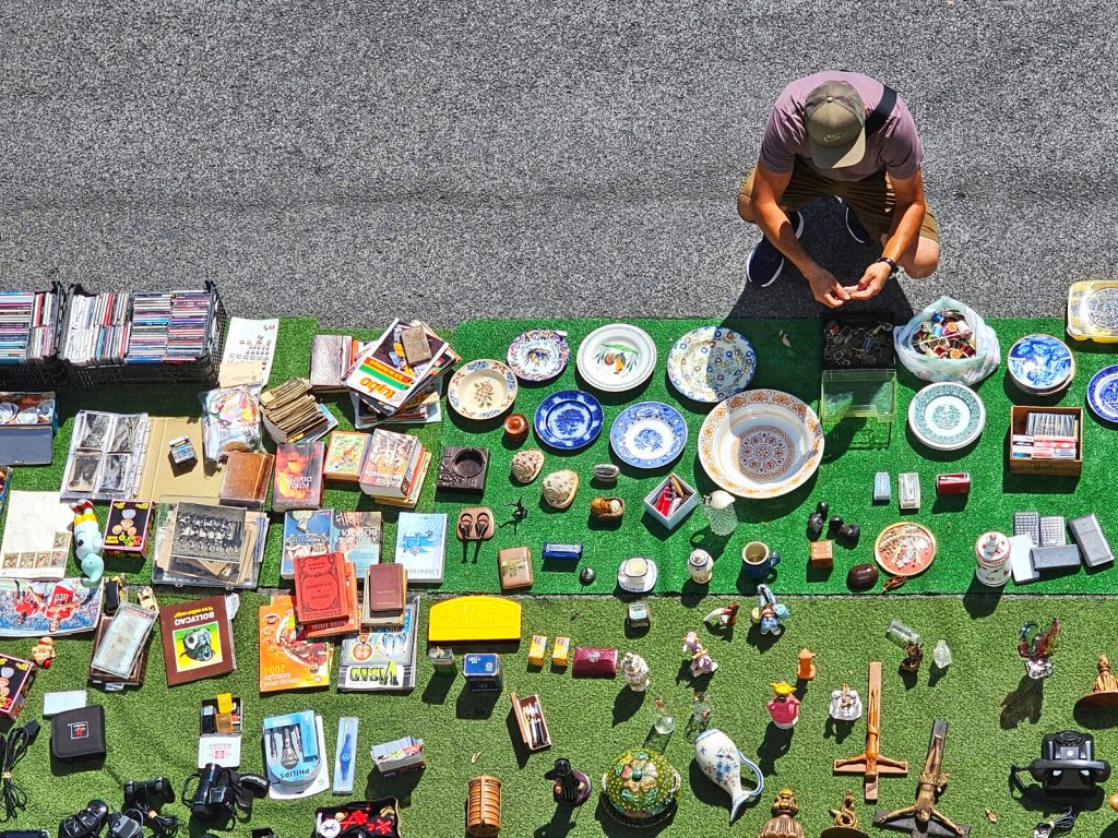Man sitting on the street looking at kniknacks on a carpet on the ground.