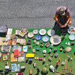 Man sitting on the street looking at kniknacks on a carpet on the ground.