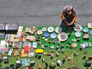 Man sitting on the street looking at kniknacks on a carpet on the ground.