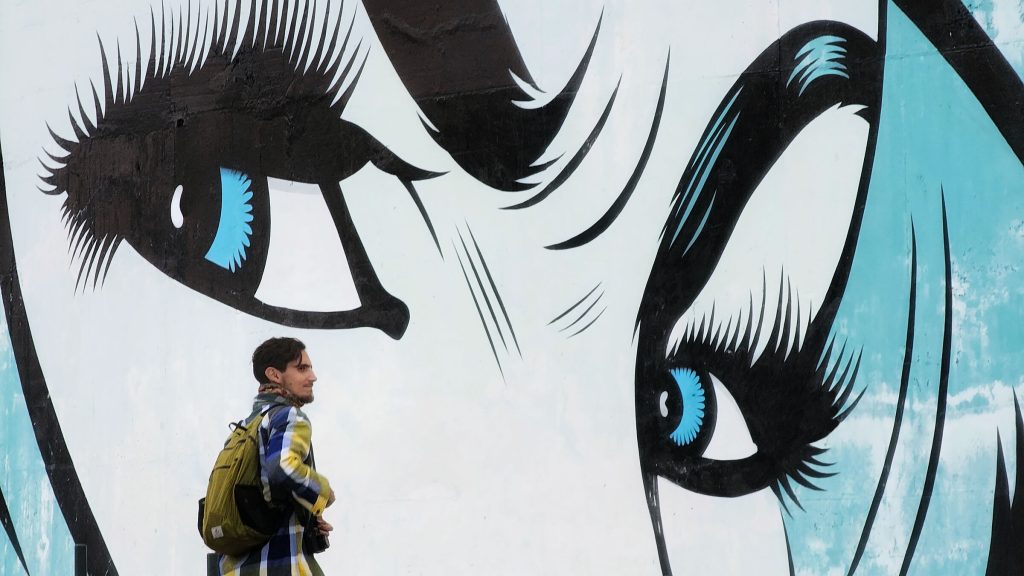 One man standing in front of a mural of a women's face - focusing on the eyes