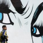 One man standing in front of a mural of a women's face - focusing on the eyes