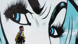 One man standing in front of a mural of a women's face - focusing on the eyes